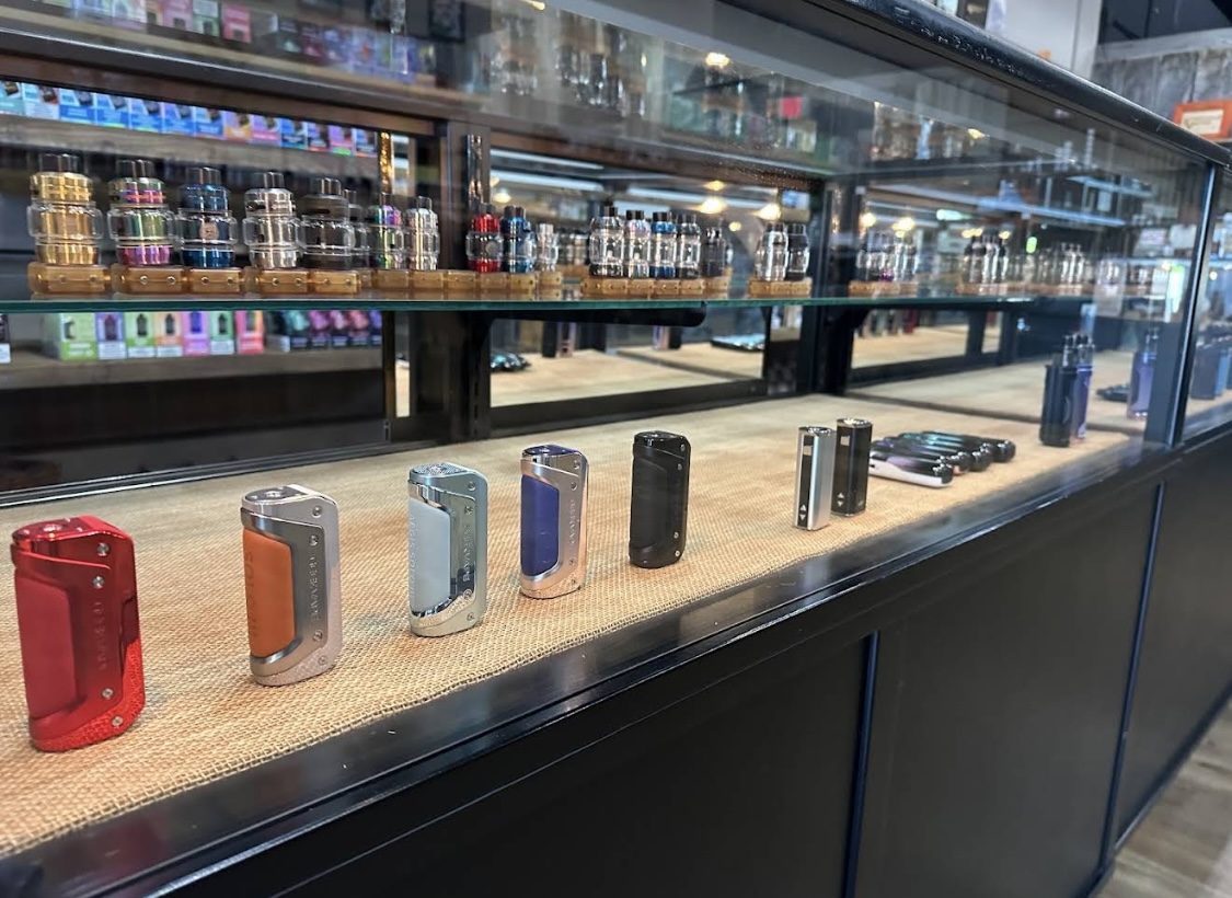 Box mods lined up on a burlap shelf in a glass display case